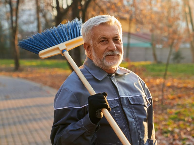 Portrait of smiling maintenance worker with broom on shoulder.
