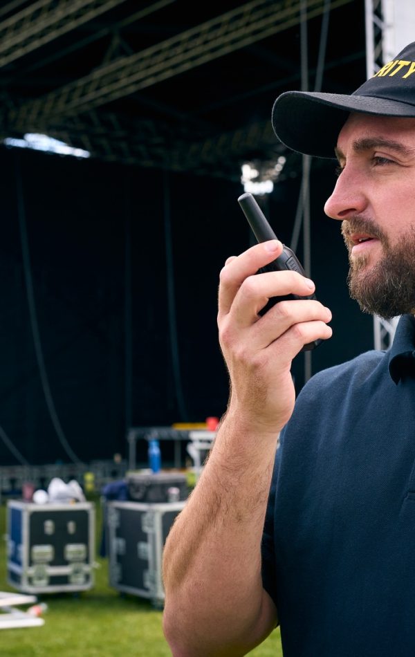 Security Team At Outdoor Stage For Music Festival Or Concert Talking Into Radio